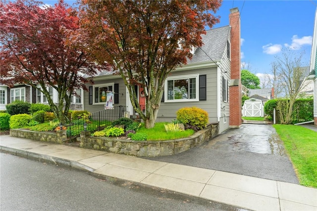 obstructed view of property with a chimney, an outbuilding, roof with shingles, and asphalt driveway
