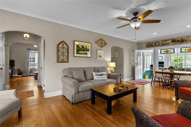 living room with arched walkways, a ceiling fan, wood finished floors, ornamental molding, and baseboards