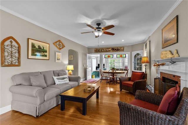 living area with crown molding, ceiling fan, wood finished floors, arched walkways, and a fireplace