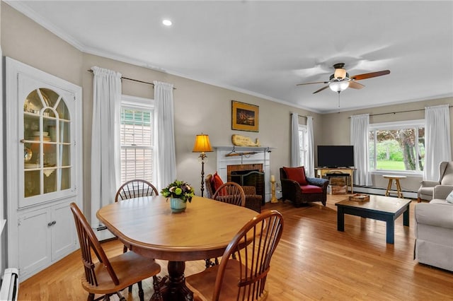 dining space featuring plenty of natural light, baseboard heating, a fireplace, light wood-type flooring, and ornamental molding