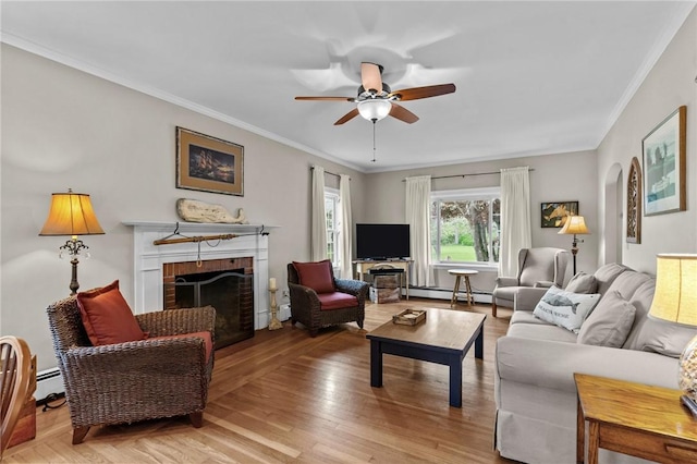 living area featuring a baseboard heating unit, a ceiling fan, a fireplace, ornamental molding, and light wood finished floors
