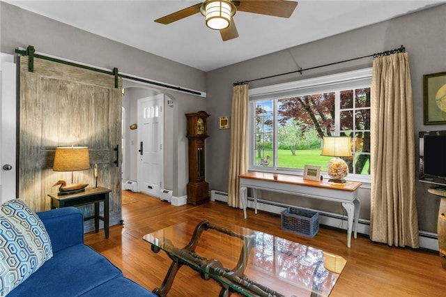 living area featuring ceiling fan, a barn door, wood finished floors, and a baseboard heating unit