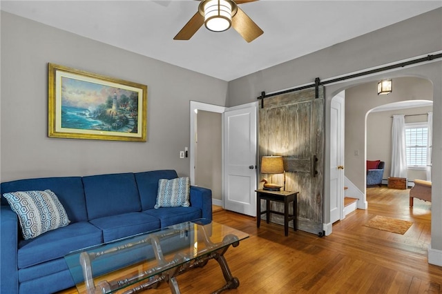 living area with arched walkways, ceiling fan, wood finished floors, and a barn door
