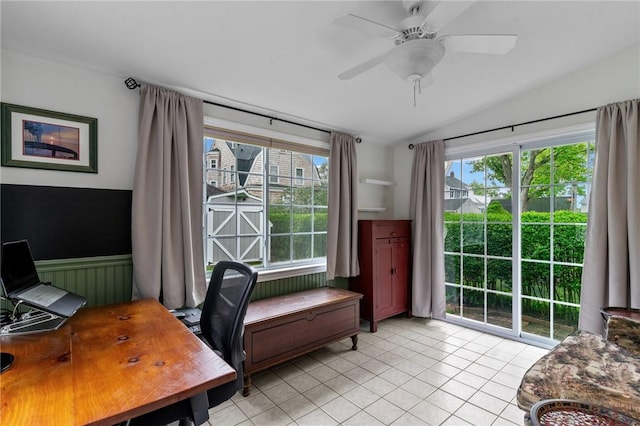 home office with lofted ceiling, a ceiling fan, light tile patterned flooring, and a wainscoted wall