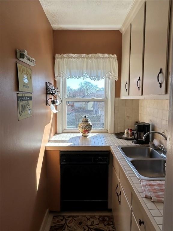kitchen featuring tile counters, dishwasher, a sink, decorative backsplash, and a textured ceiling