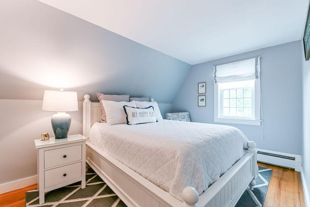 bedroom featuring a baseboard heating unit, vaulted ceiling, wood finished floors, and baseboards