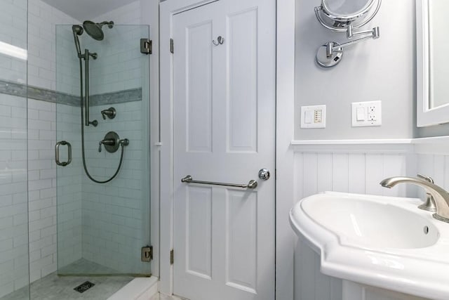 bathroom featuring a stall shower, a sink, and wainscoting
