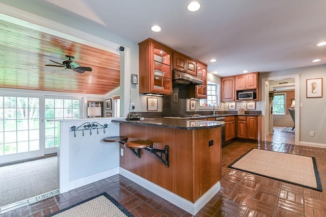 kitchen with stainless steel microwave, a peninsula, glass insert cabinets, baseboards, and under cabinet range hood