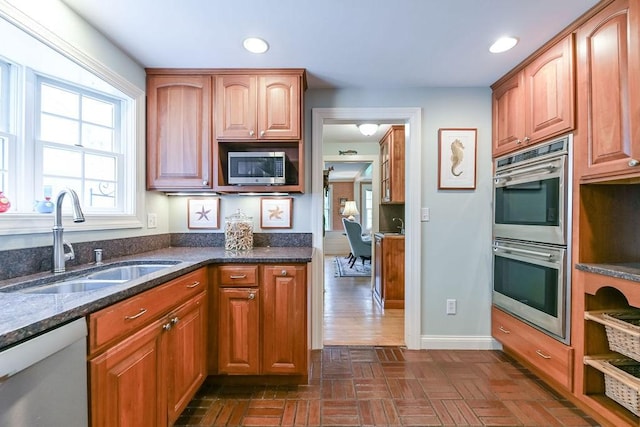 kitchen with appliances with stainless steel finishes, a sink, dark stone counters, recessed lighting, and baseboards