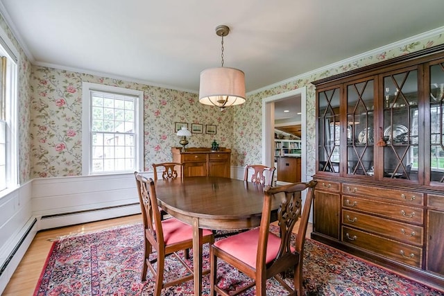 dining space featuring wallpapered walls, light wood-style flooring, a wainscoted wall, a baseboard radiator, and ornamental molding