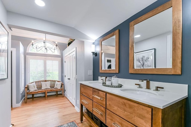 bathroom featuring vaulted ceiling, wood finished floors, a baseboard heating unit, double vanity, and a chandelier