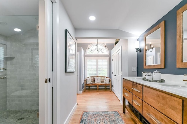 full bath with lofted ceiling, tiled shower, wood finished floors, double vanity, and a chandelier