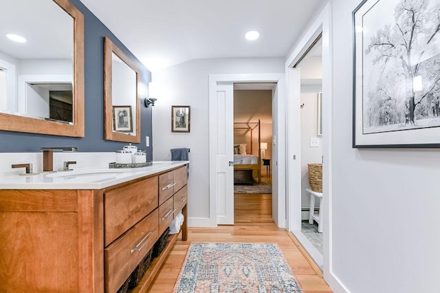 full bath featuring a baseboard heating unit, wood finished floors, ensuite bath, double vanity, and recessed lighting
