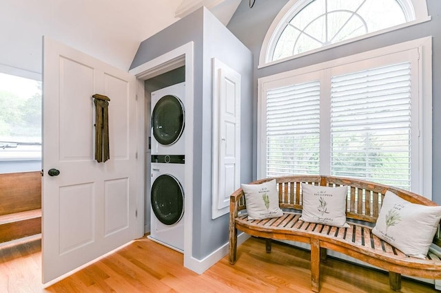 clothes washing area with stacked washer / dryer, light wood finished floors, and baseboards