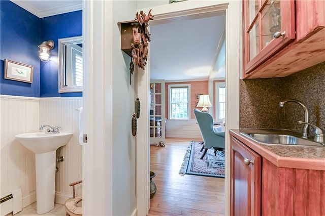 hallway featuring a sink, baseboard heating, light wood-type flooring, a wainscoted wall, and crown molding