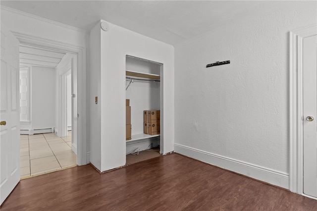 unfurnished bedroom with baseboard heating, wood finished floors, and a closet