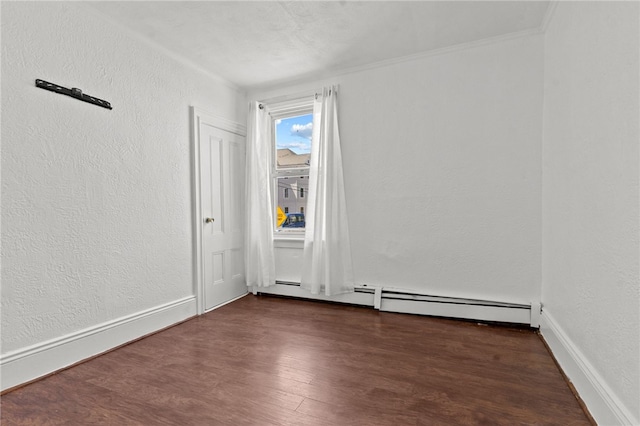 empty room with dark wood-style flooring, a baseboard heating unit, a textured wall, and baseboards