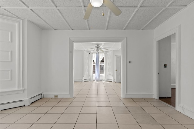 empty room featuring a ceiling fan, baseboard heating, light tile patterned floors, and baseboards