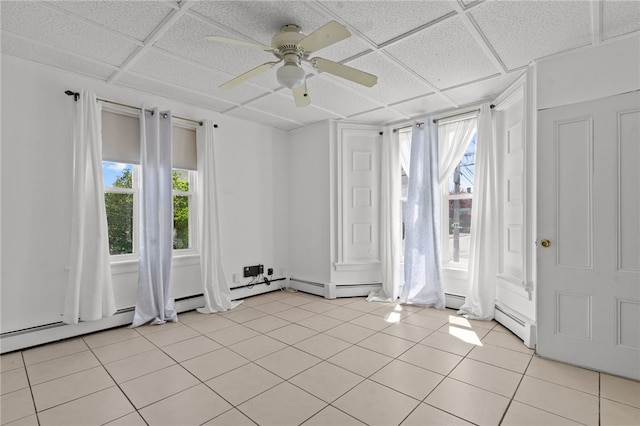 unfurnished room with healthy amount of natural light, ceiling fan, a drop ceiling, and light tile patterned floors