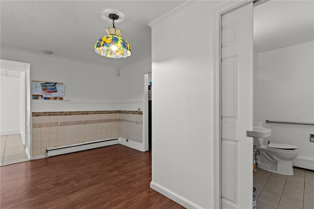 unfurnished dining area with a baseboard radiator, crown molding, wood finished floors, and baseboards