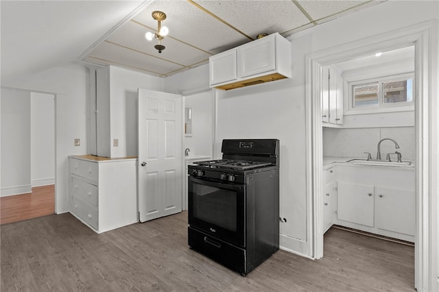 kitchen featuring black gas range oven, a sink, white cabinets, light wood finished floors, and light countertops