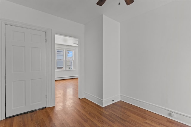 empty room with baseboard heating, ceiling fan, wood finished floors, and baseboards