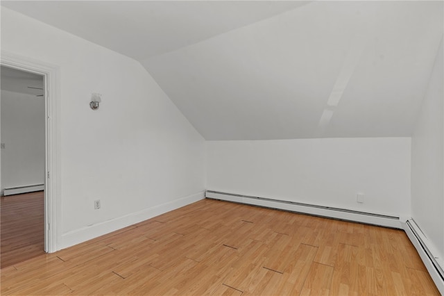 additional living space with baseboard heating, vaulted ceiling, light wood-type flooring, and baseboards