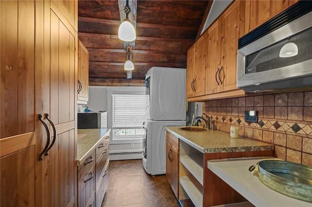 275 Hope St, Bristol, RI 02809 - kitchen with stainless steel microwave, a baseboard heating unit, stacked washing machine and dryer, decorative backsplash, and dark tile patterned flooring