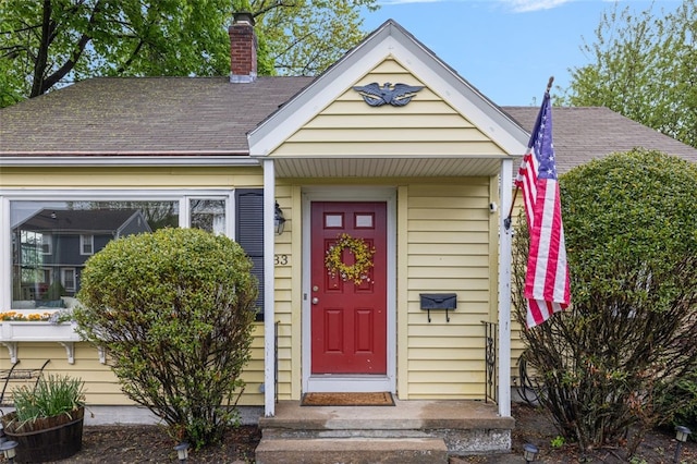 entrance to property with roof with shingles and a chimney