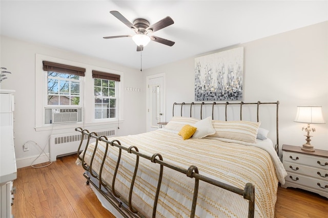 bedroom with radiator, cooling unit, light wood-type flooring, baseboards, and ceiling fan
