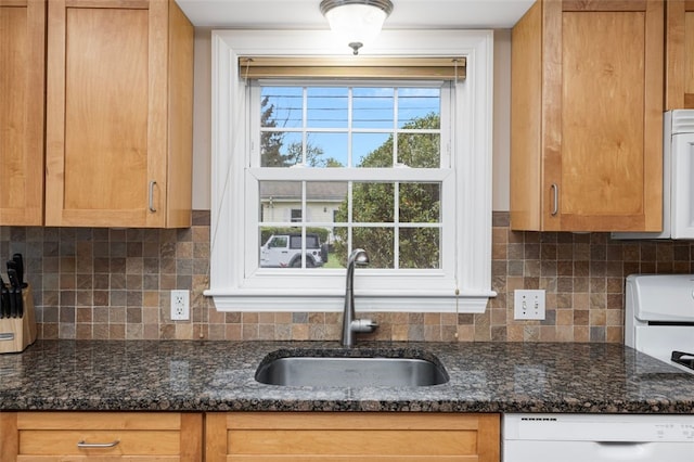 kitchen with dishwasher, a sink, dark stone counters, and decorative backsplash