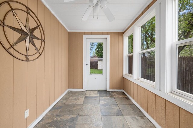 unfurnished sunroom featuring baseboards, stone finish floors, and wooden walls