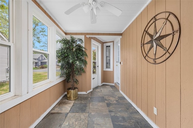 unfurnished sunroom with stone finish flooring, wooden walls, and baseboards