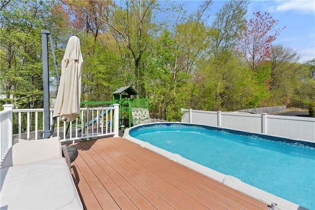 outdoor pool featuring a wooden deck, a playground, and fence