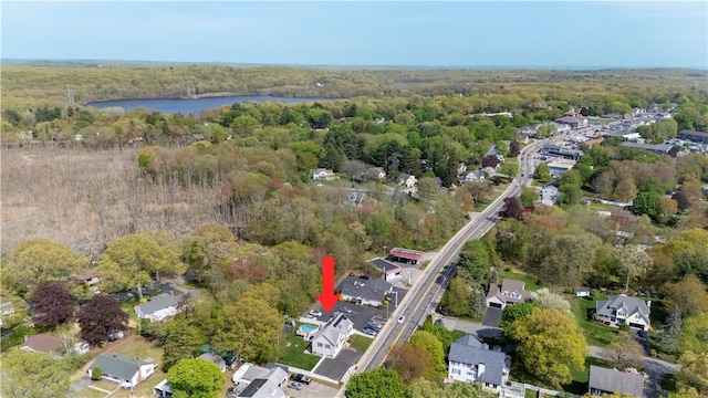 aerial view of property and surrounding area featuring a forest, a nearby body of water, and nearby suburban area