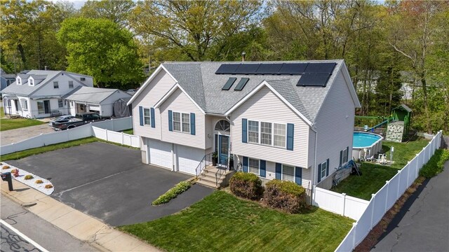 raised ranch with a garage, solar panels, roof with shingles, asphalt driveway, and view of wooded area