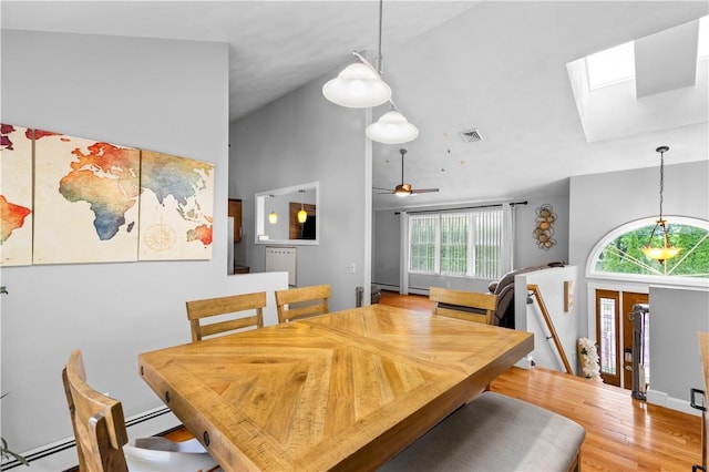 dining area featuring a skylight, plenty of natural light, a baseboard heating unit, a towering ceiling, and wood finished floors