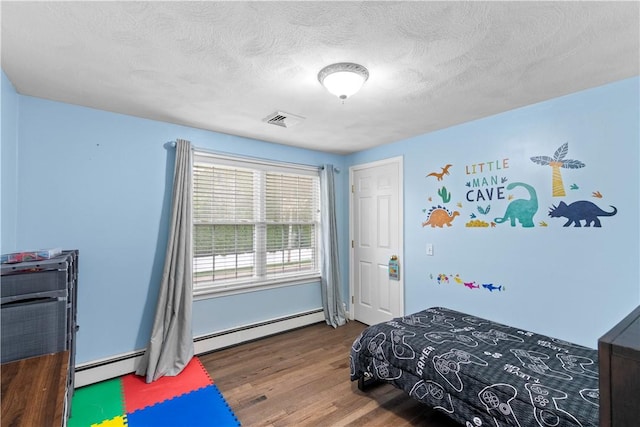 bedroom featuring a baseboard heating unit, wood finished floors, and a textured ceiling