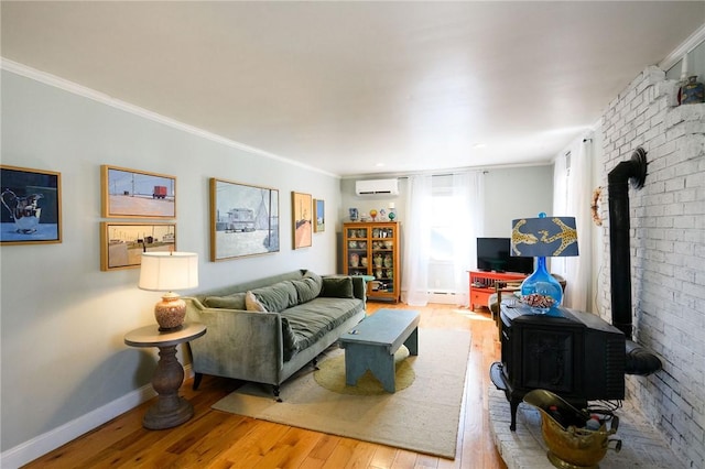 living area featuring a wood stove, a wall mounted air conditioner, wood-type flooring, ornamental molding, and baseboards
