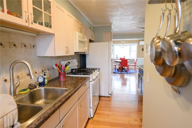 kitchen with white appliances, a sink, crown molding, light wood-style flooring, and glass insert cabinets