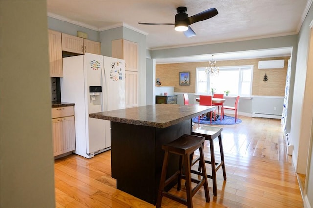kitchen with white fridge with ice dispenser, a baseboard heating unit, dark countertops, light wood-style flooring, and a breakfast bar