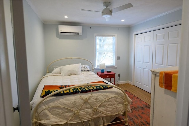 bedroom featuring an AC wall unit, crown molding, wood finished floors, baseboards, and a closet