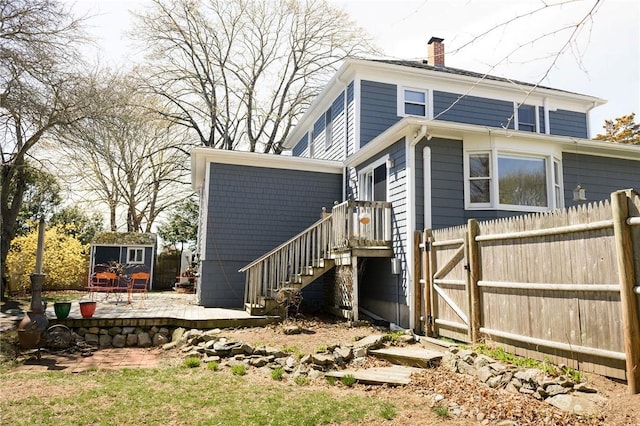 rear view of property with a chimney, a patio area, fence, an outdoor structure, and a gate