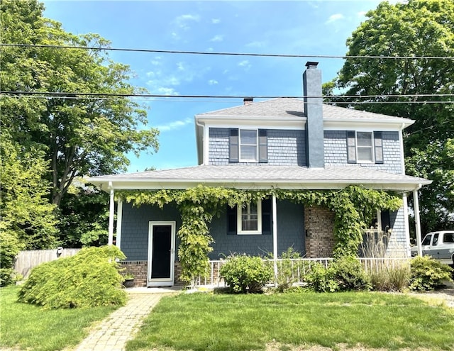 view of front of property featuring a porch, a chimney, a front yard, and roof with shingles