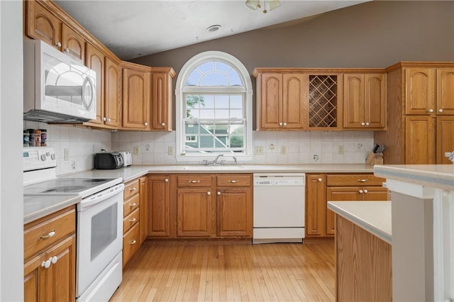 kitchen featuring white appliances, lofted ceiling, light wood-style flooring, light countertops, and a sink