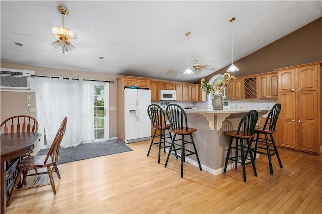 kitchen featuring white appliances, a ceiling fan, light wood-style floors, vaulted ceiling, and a breakfast bar