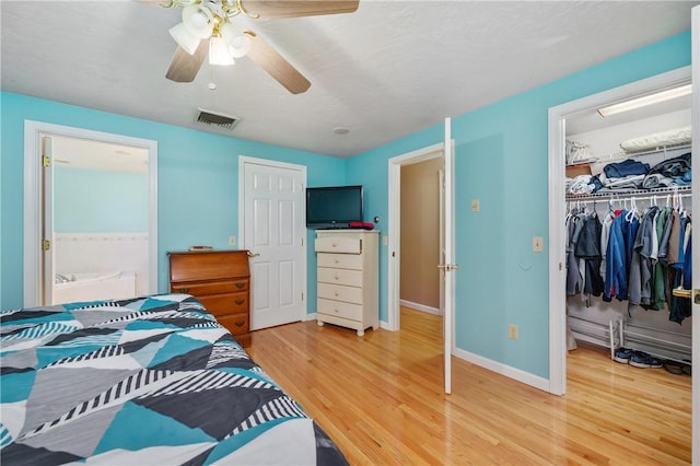 bedroom with wood finished floors, a closet, a walk in closet, baseboards, and ceiling fan
