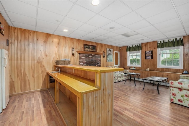bar with light wood finished floors, wooden walls, baseboard heating, and a paneled ceiling
