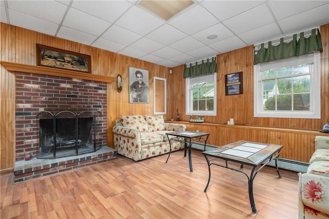 living area with a drop ceiling, a fireplace, wooden walls, wood finished floors, and a baseboard radiator