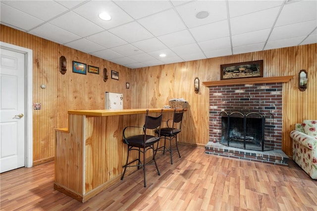 indoor dry bar with light wood finished floors, freestanding refrigerator, baseboards, a fireplace, and wood walls